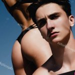 Beautiful young couple of lovers isolated at clear blue sky background. Sexy hot woman with fit sexy ass in bikini standing behind her handsome boyfriend. Sexy desire and love concept. Stock
