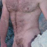 A playful sexy and hairy man poses behind a rock shows his naked body. Bath Towel by Gunther Allen